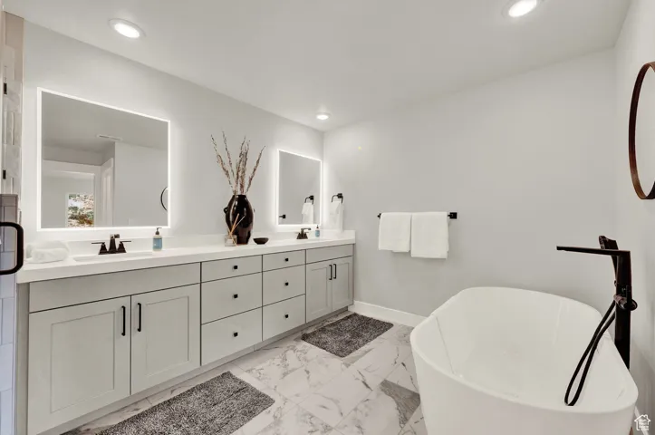 Full bath featuring double vanity, a soaking tub, marble look tiles, recessed lighting, and baseboards