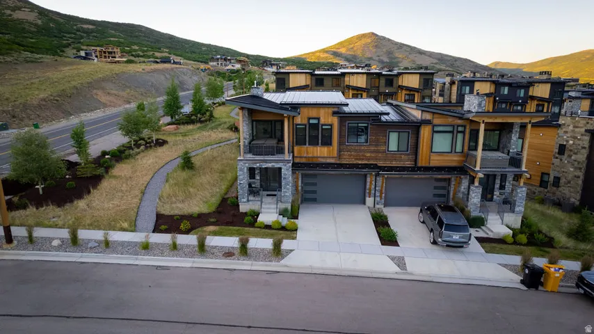 Contemporary architectural design featuring stone and natural wood siding, multiple balconies, a covered entryway, and two-car garage