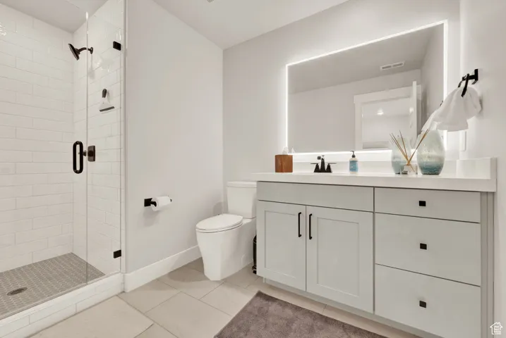 Bathroom featuring vanity, a stall shower, toilet, baseboards, and tile patterned floors