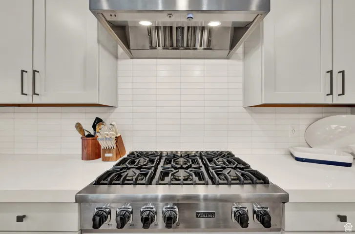 Kitchen featuring wall chimney range hood, light countertops, backsplash, and stainless steel gas stovetop