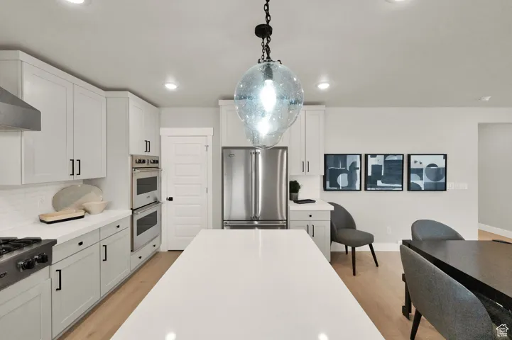 Kitchen with appliances with stainless steel finishes, light wood finished floors, backsplash, light countertops, and recessed lighting