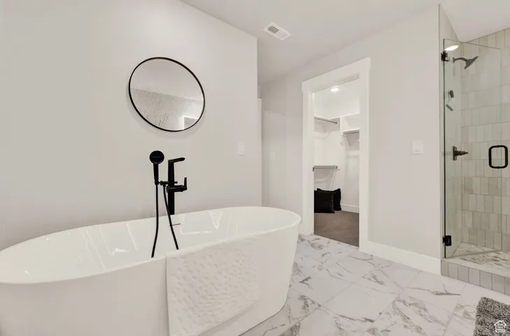 Bathroom with a spacious closet, a shower stall, marble finish floors, a soaking tub, and baseboards