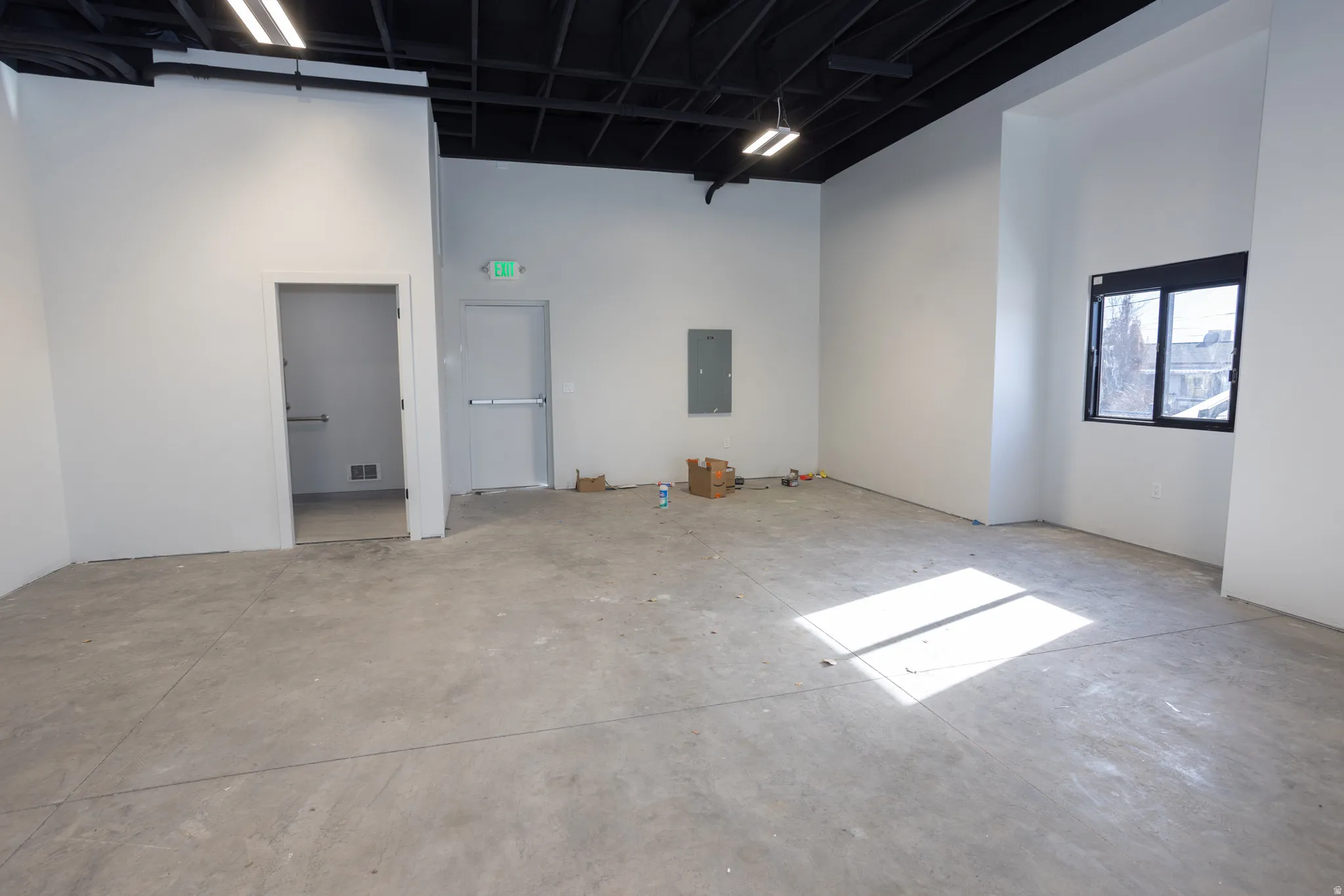 Unfurnished room with electric panel, concrete floors, and a high ceiling