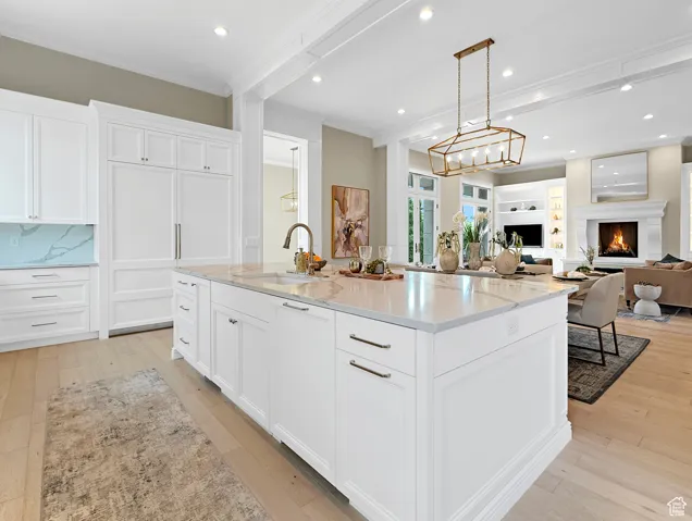 Kitchen with a sink, ornamental molding, a center island with sink, white cabinets, and light wood-type flooring
