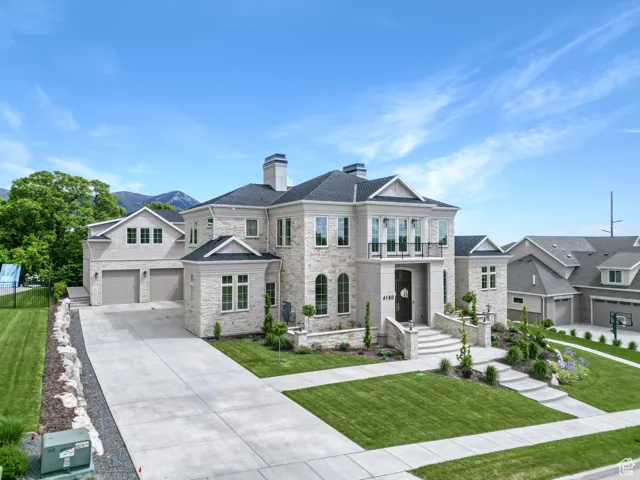View of front facade featuring stone siding, a chimney, an attached garage, driveway, and a balcony
