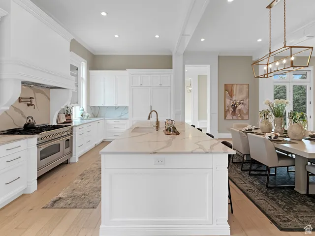 Kitchen featuring oven range, a sink, crown molding, light wood-style floors, and a chandelier