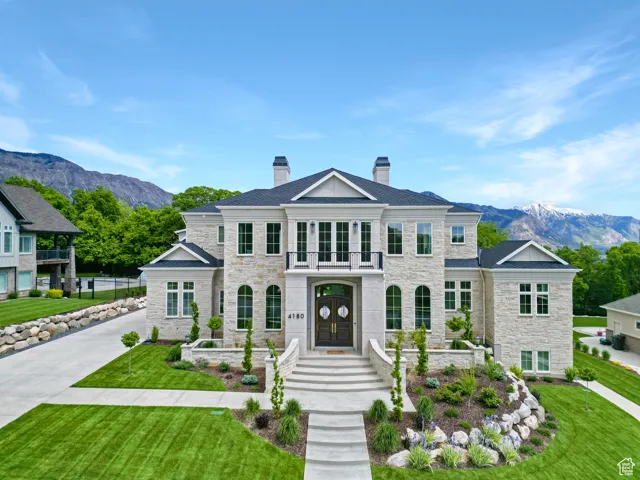 View of front of property featuring stone siding, a balcony, a chimney, a mountain view, and a front yard