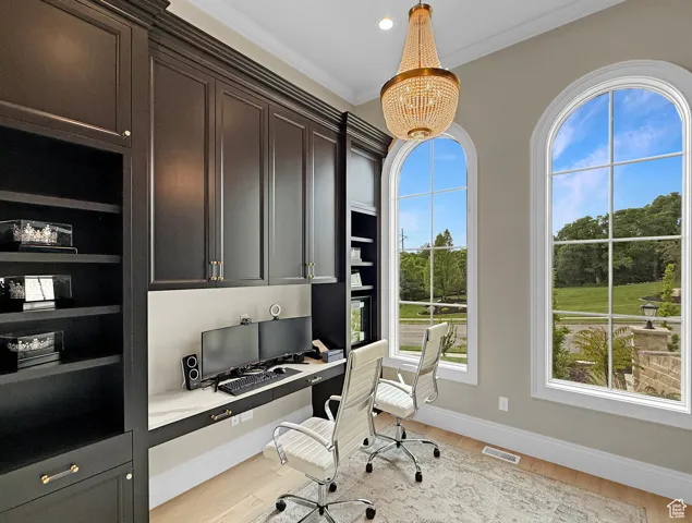 Home office with built in study area, baseboards, ornamental molding, light wood-style floors, and a chandelier