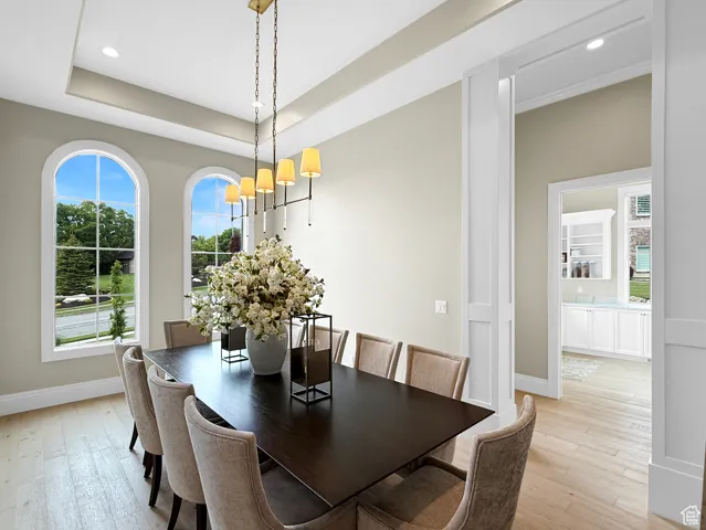Dining area with a chandelier, baseboards, light wood-style floors, recessed lighting, and a raised ceiling
