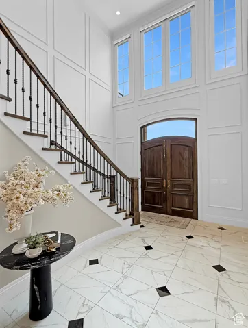 Entryway with marble finish flooring, a towering ceiling, stairs, a decorative wall, and baseboards