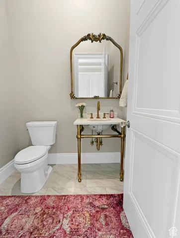 Half bath with marble look tiles, toilet, and baseboards