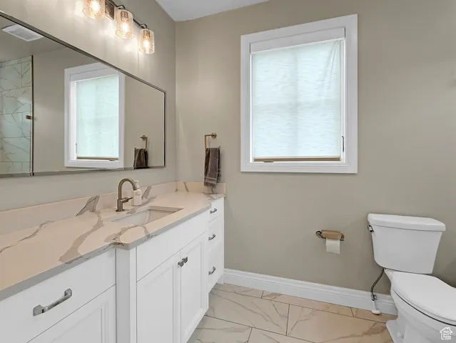 Full bathroom with marble finish floors, toilet, vanity, and baseboards