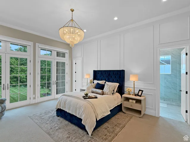 Carpeted bedroom featuring a decorative wall, access to exterior, a chandelier, ornamental molding, and french doors