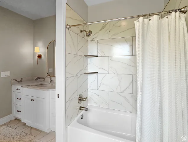 Full bathroom featuring shower / bath combo with shower curtain, vanity, and marble look tiles