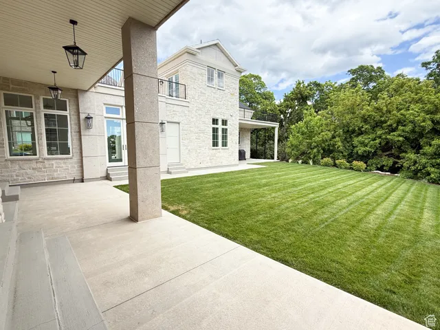 View of green lawn with a balcony and a patio