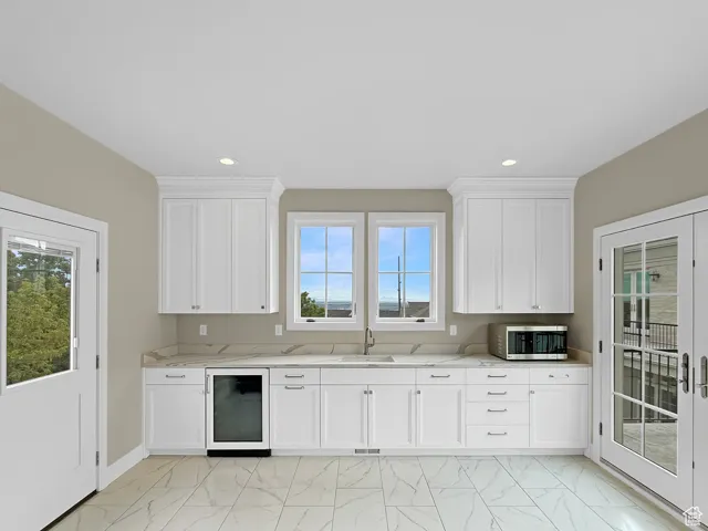 Above garage kitchen with beverage cooler, stainless steel microwave, light marble finish flooring, a sink, and plenty of natural light