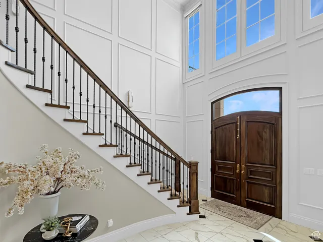 Foyer featuring marble look tile flooring, a decorative wall, a towering ceiling, baseboards, and stairway