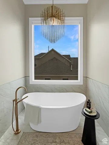 Full bath with tile walls, a soaking tub, marble finish floors, a chandelier, and crown molding