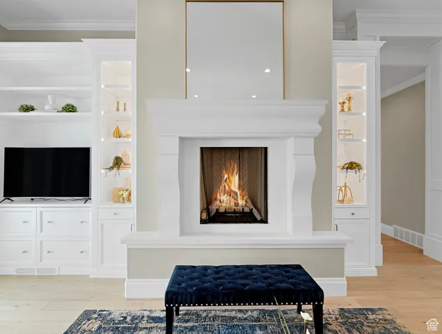 Detailed view of wood finished floors, ornamental molding, a warm lit fireplace, and baseboards