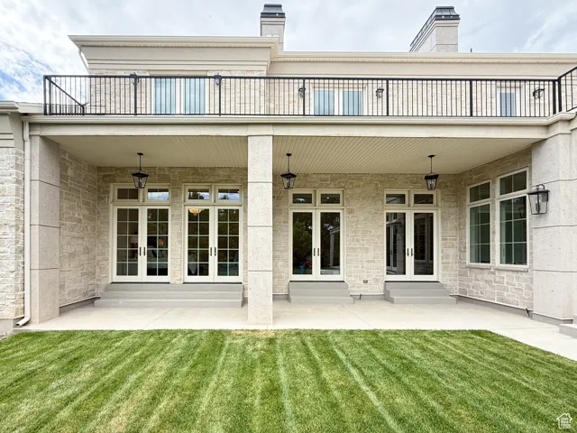 Rear view of house featuring french doors, a balcony, a yard, and stone siding