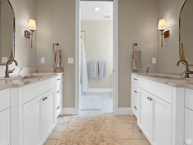 Bathroom with marble look tiles, baseboards, two vanities, recessed lighting, and a shower with shower curtain