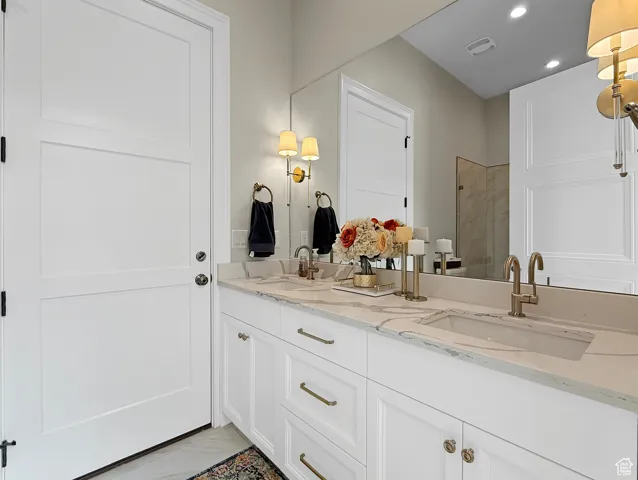 Bathroom featuring marble finish flooring, double vanity, recessed lighting, and a tile shower