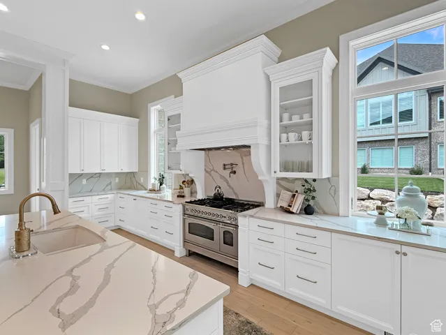Kitchen with a sink, range with two ovens, recessed lighting, glass insert cabinets, and ornamental molding
