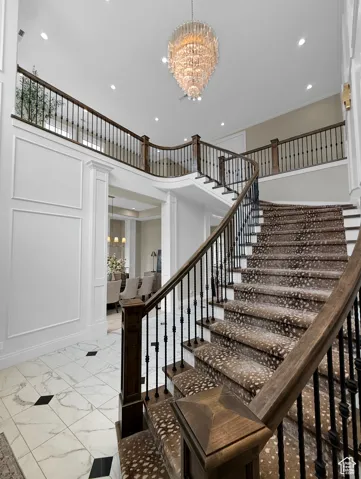 Staircase with a chandelier, marble look tiles, recessed lighting, and a decorative wall