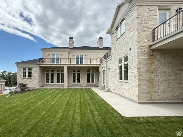 Rear view of property with a balcony, french doors, a yard, a patio area, and a chimney