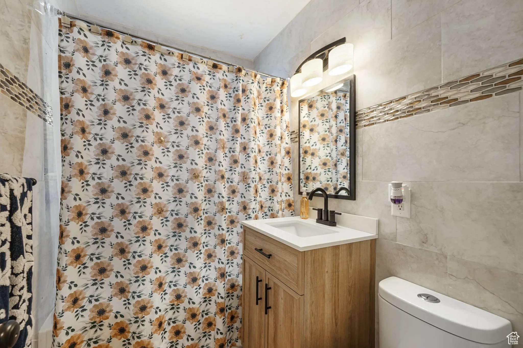 Full bathroom with tile walls, vanity, toilet, and a shower with curtain