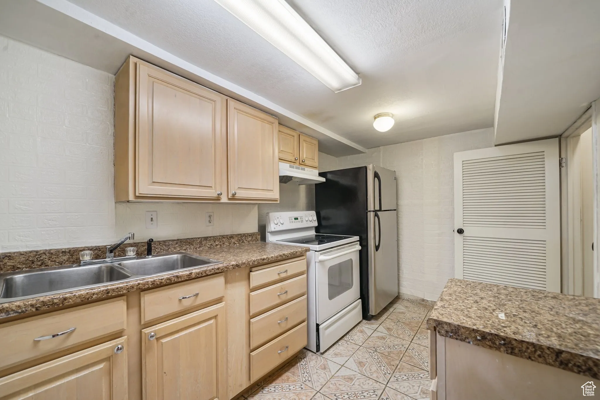 Kitchen featuring white electric stove, light brown cabinetry, under cabinet range hood, a sink, and light tile patterned flooring