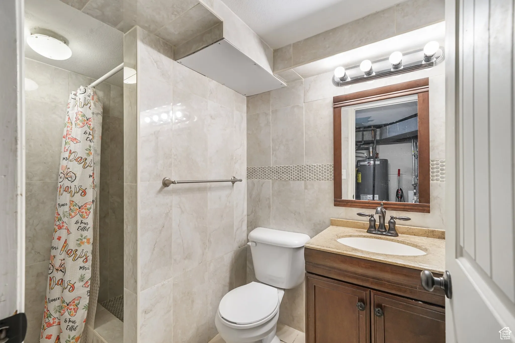 Full bath with water heater, tile walls, a stall shower, vanity, and toilet