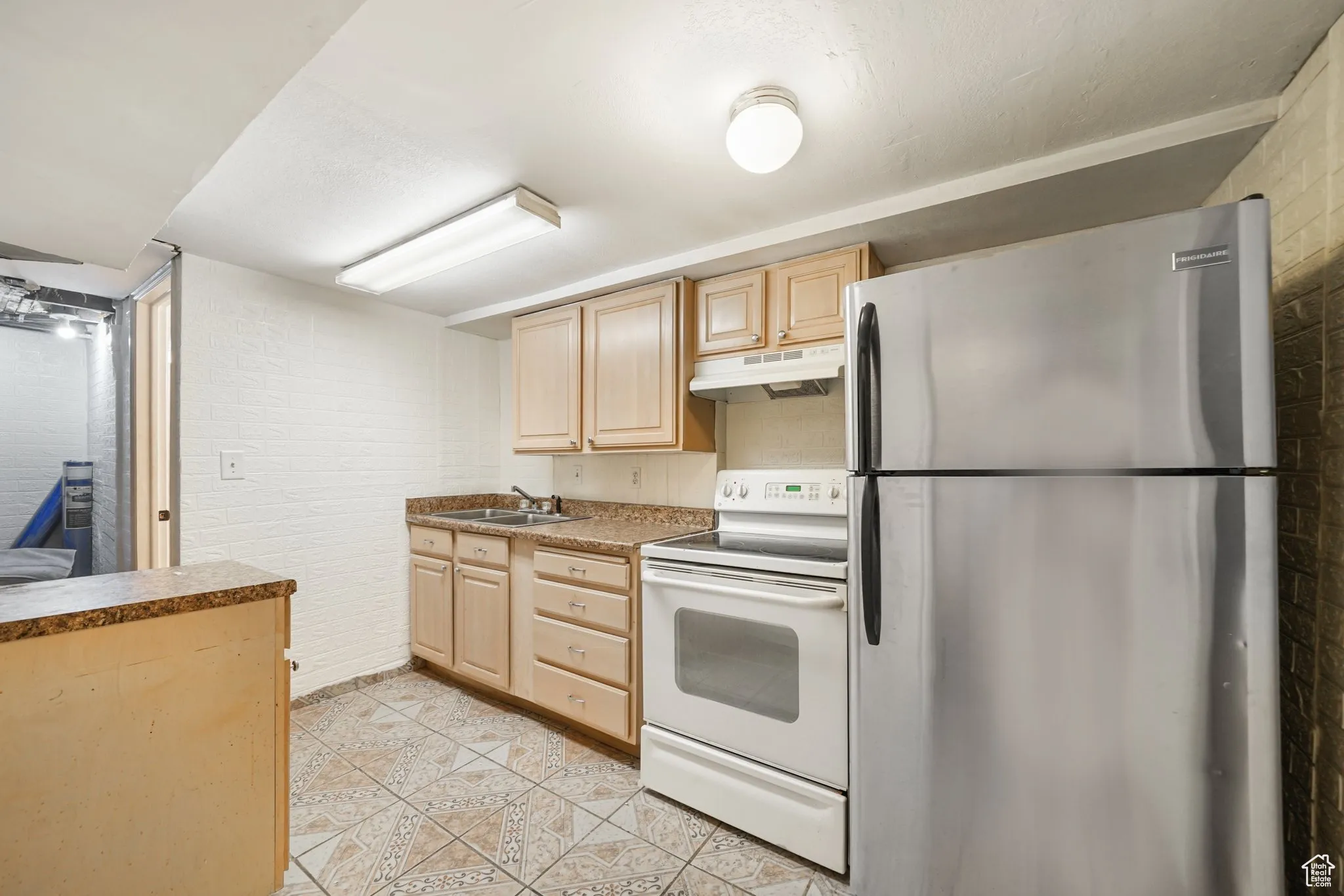 Kitchen featuring freestanding refrigerator, white electric range oven, light brown cabinets, under cabinet range hood, and a sink