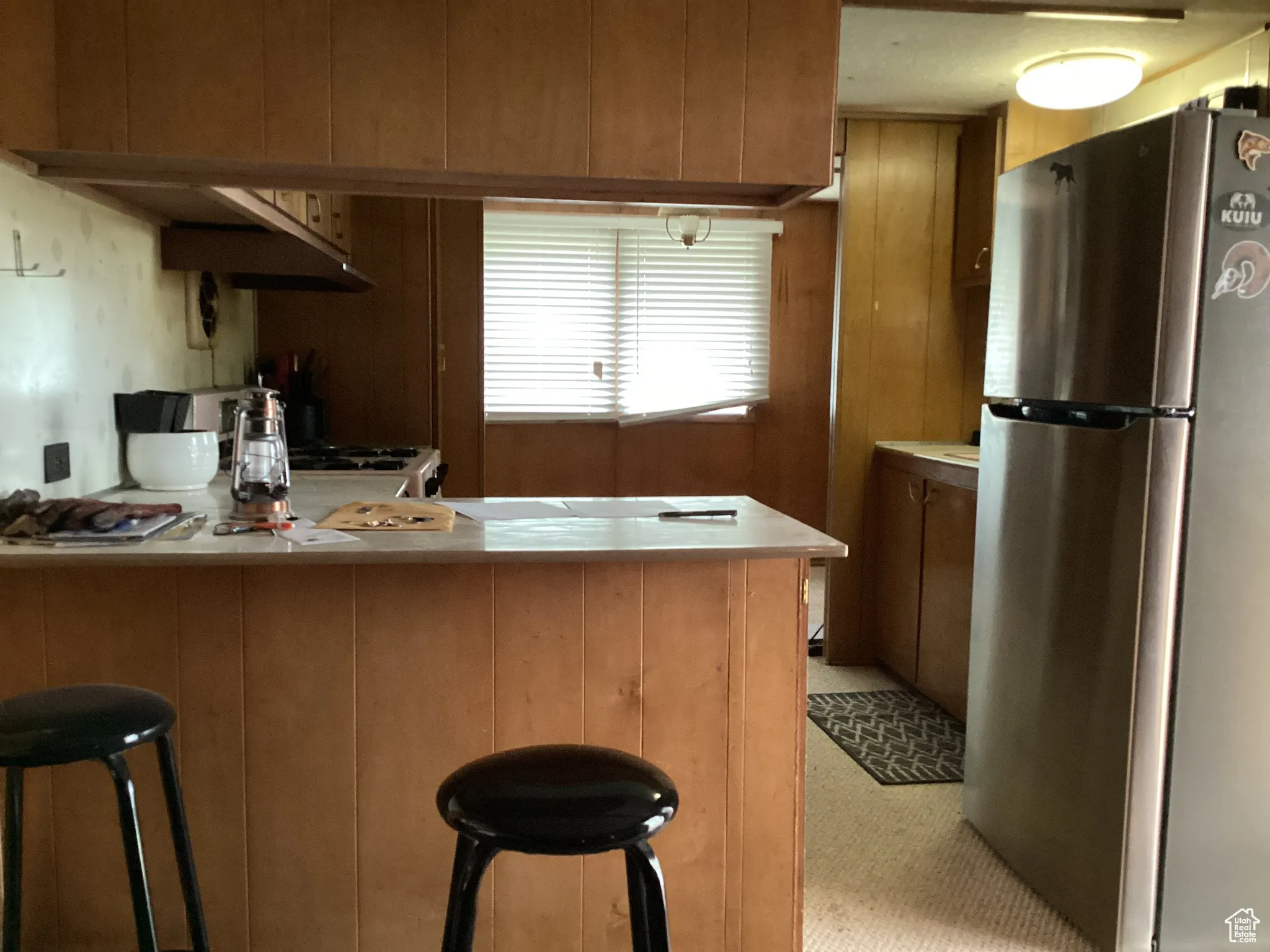 Kitchen with freestanding refrigerator, a peninsula, light countertops, a breakfast bar area, and brown cabinetry