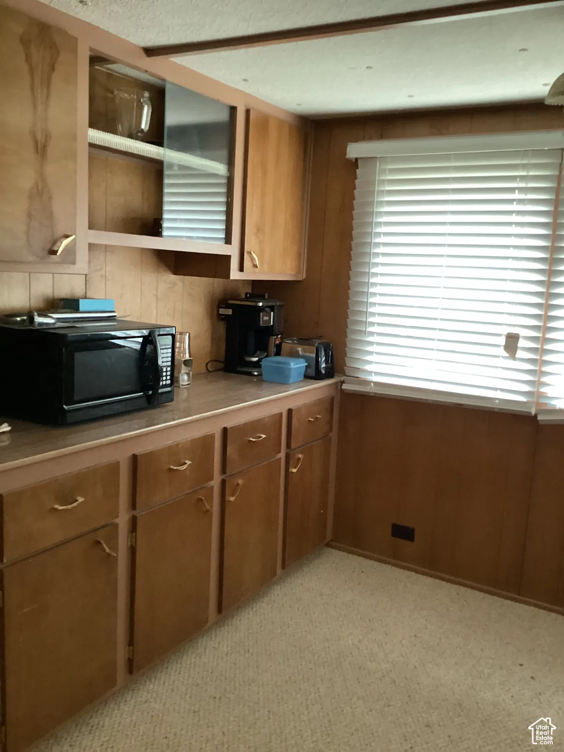 Kitchen featuring black microwave, brown cabinets, wood walls, light carpet, and light countertops