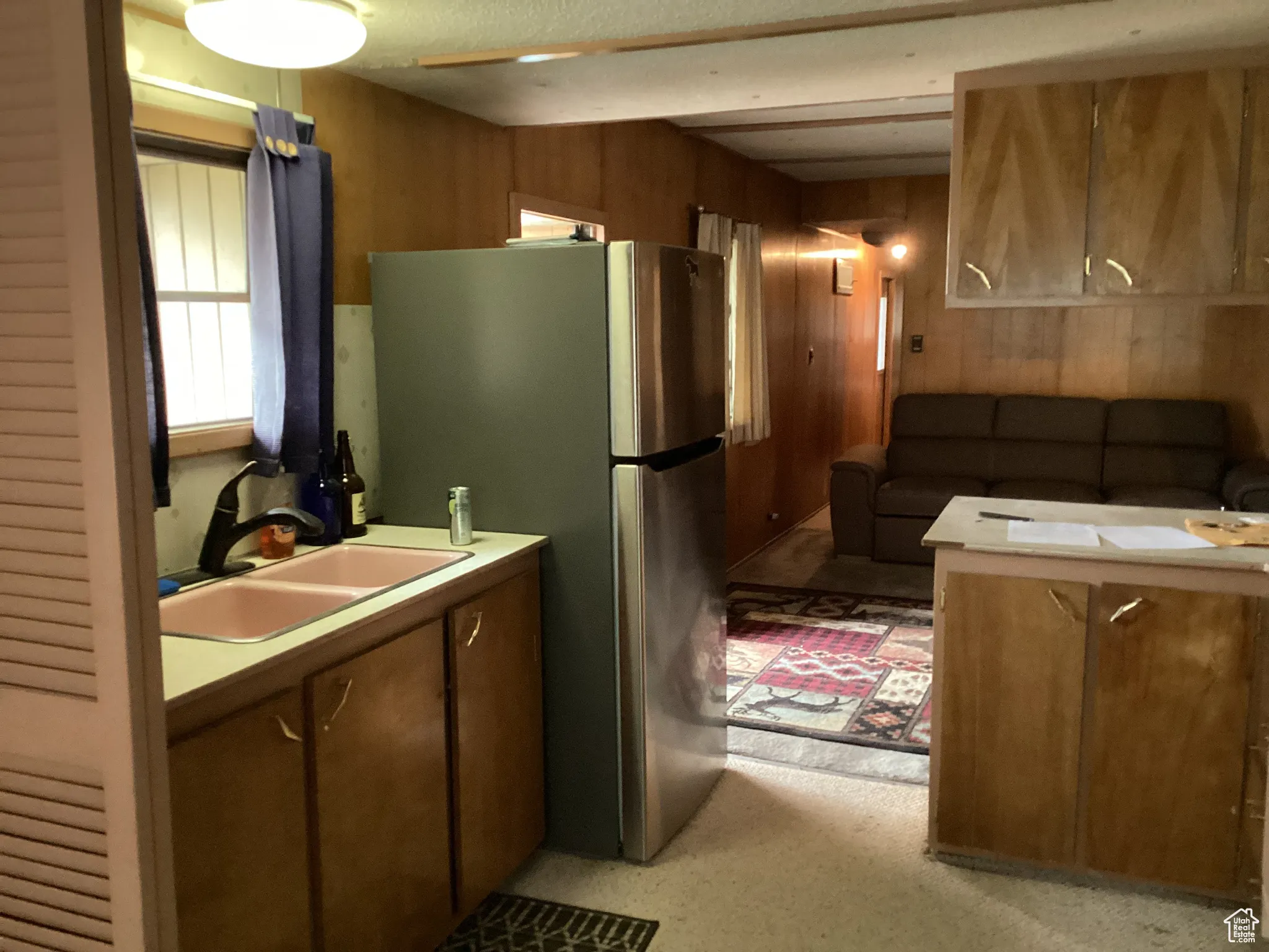 Kitchen with a sink, wooden walls, freestanding refrigerator, and light countertops