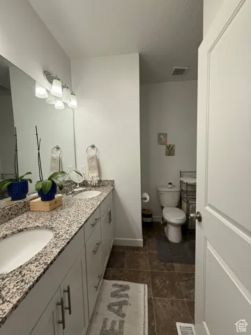 Full bathroom with toilet, baseboards, double vanity, and stone finish flooring