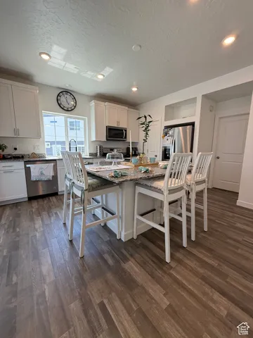 Kitchen with appliances with stainless steel finishes, dark wood-style floors, a kitchen bar, a textured ceiling, and stone countertops