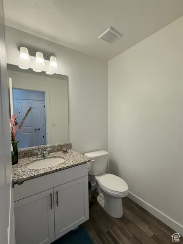 Half bathroom featuring wood finished floors, toilet, baseboards, and vanity