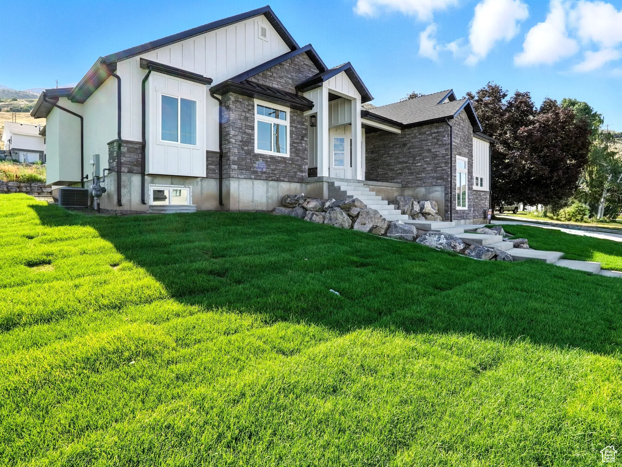View of front facade with stone siding, board and batten siding, and a front yard