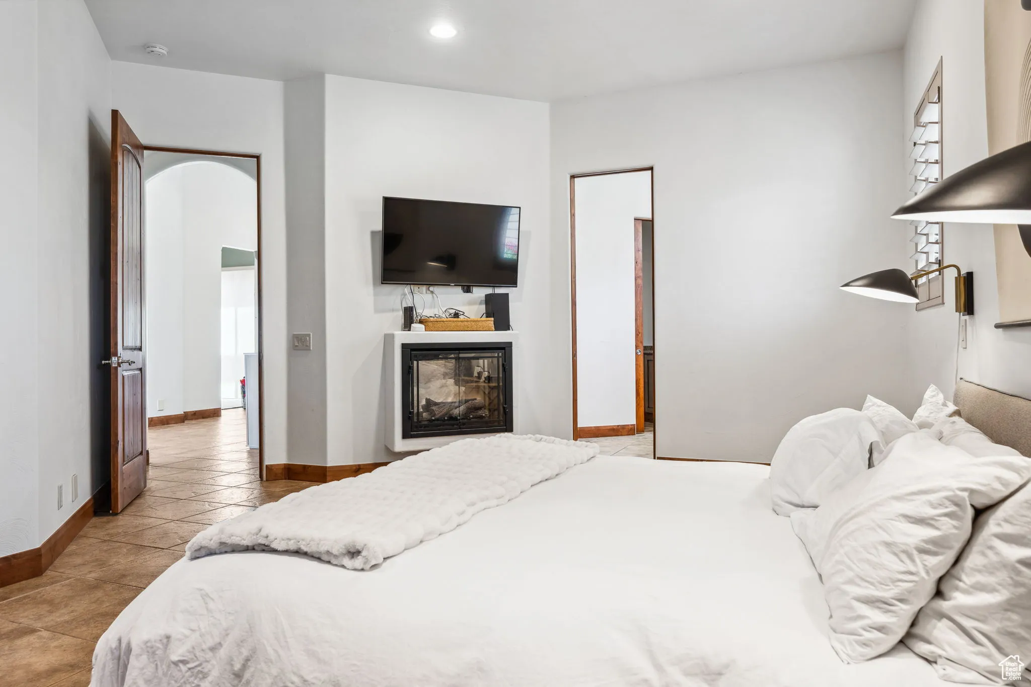 Bedroom with baseboards, a glass covered fireplace, recessed lighting, tile patterned flooring, and arched walkways