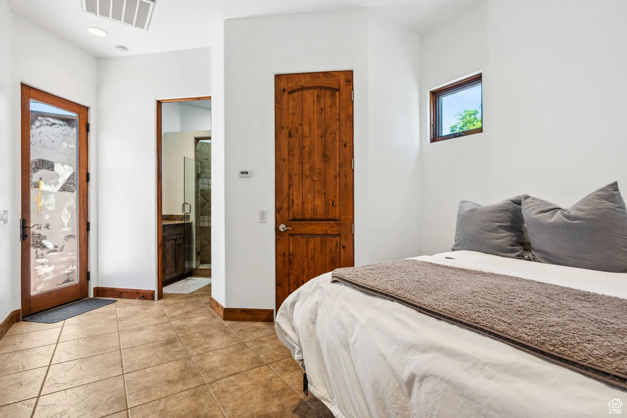 Bedroom featuring baseboards, light tile patterned flooring, and ensuite bath