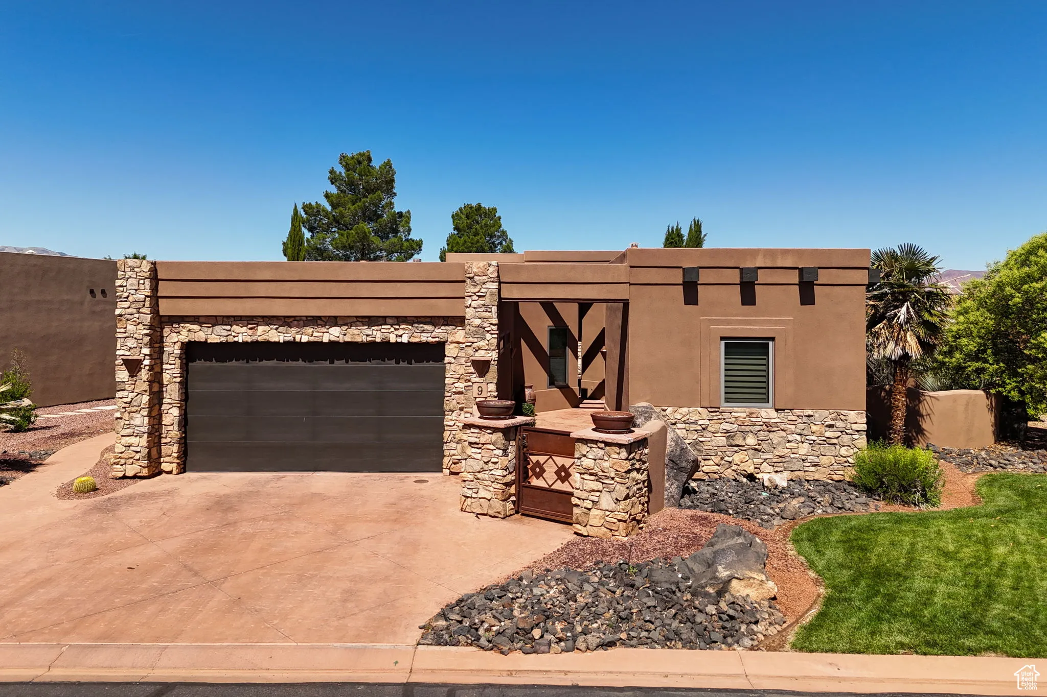 Pueblo-style house with an attached garage, concrete driveway, stone siding, and stucco siding
