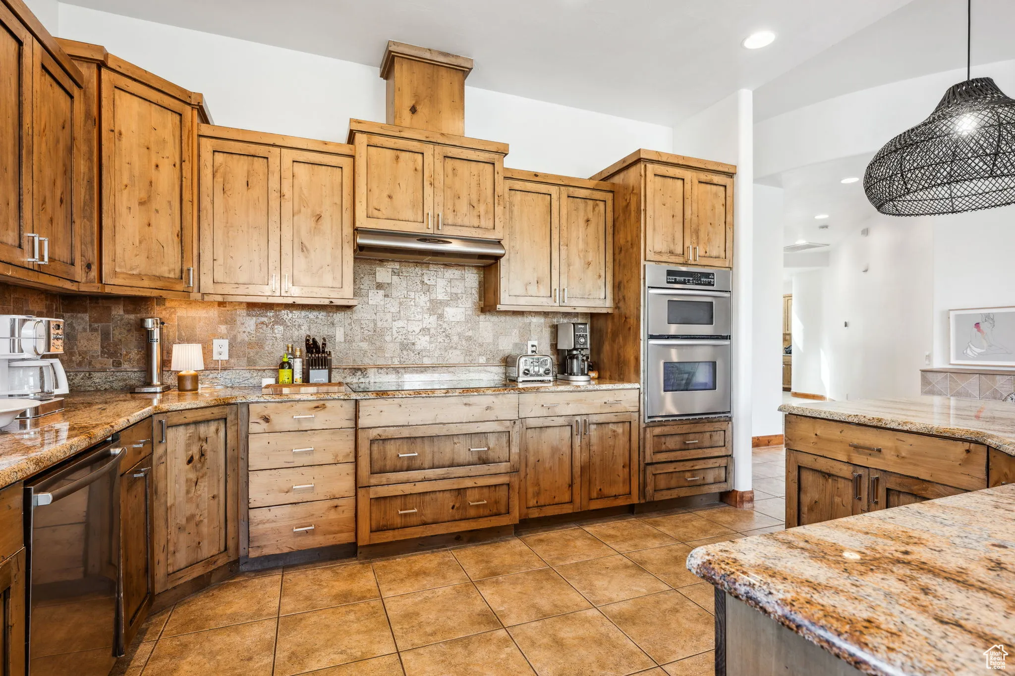 Kitchen featuring stainless steel double oven, light tile patterned floors, tasteful backsplash, pendant lighting, and light stone counters