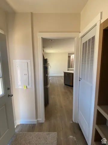 Corridor with dark wood-type flooring, baseboards, and electric panel