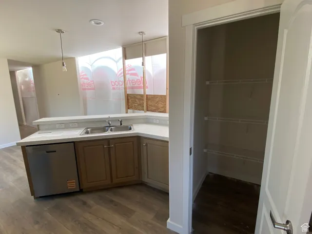 Kitchen with stainless steel dishwasher, a sink, dark wood-type flooring, light countertops, and recessed lighting