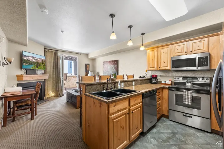 Kitchen featuring stainless steel appliances, a sink, a peninsula, decorative light fixtures, and a kitchen bar