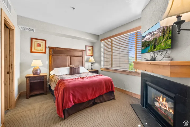 Carpeted bedroom with a glass covered fireplace, baseboards, and a textured wall