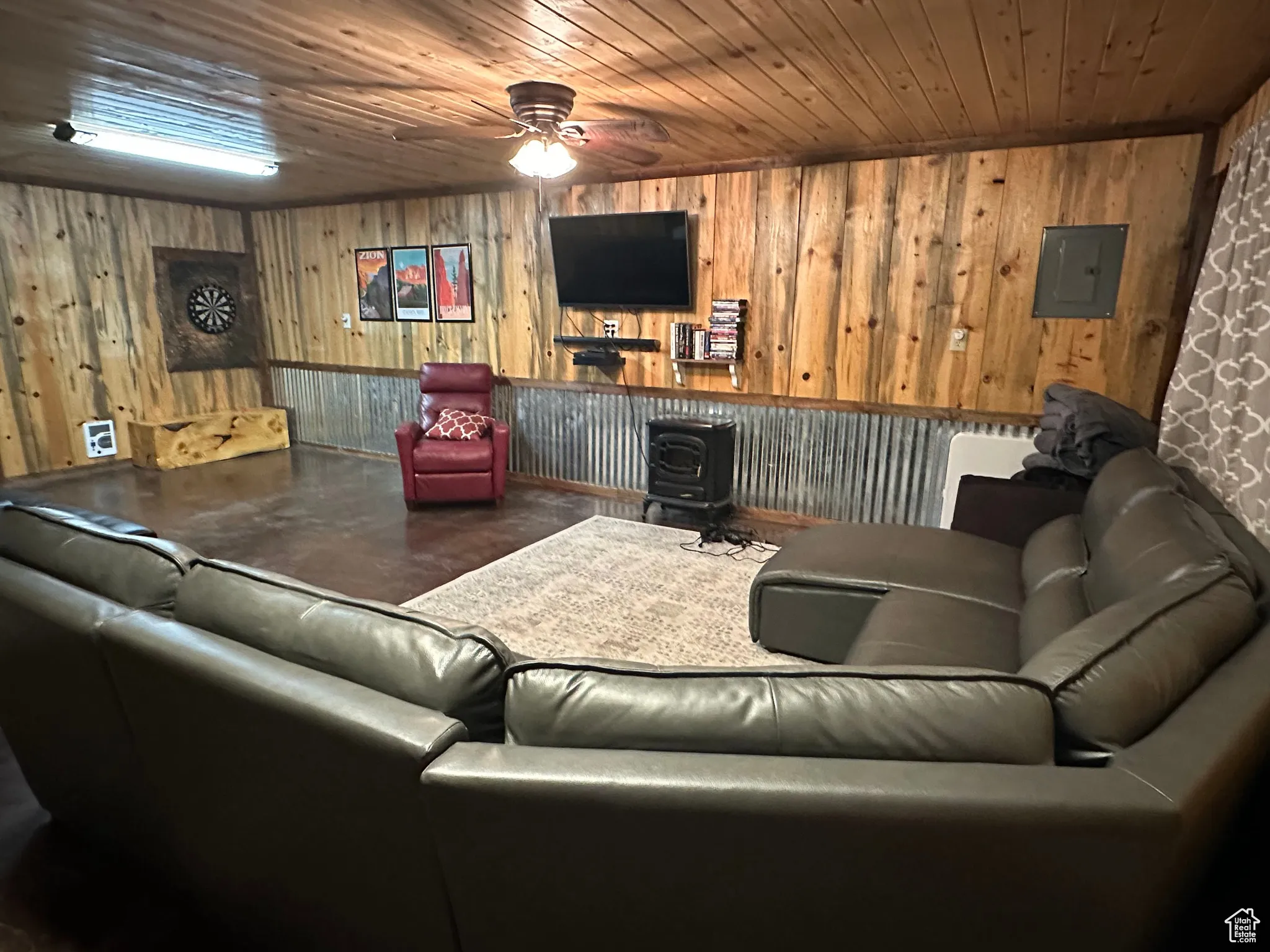 Living area with a wood stove, wood ceiling, a ceiling fan, electric panel, and concrete flooring