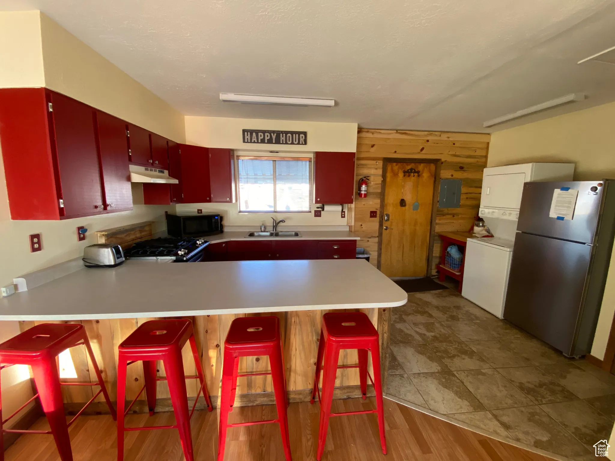 Kitchen with freestanding refrigerator, under cabinet range hood, black microwave, a sink, and red cabinetry